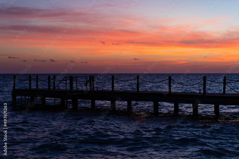 Fototapeta premium Rope bridge silhouette at sunset. Beautiful seascape, bright orange sky and sea