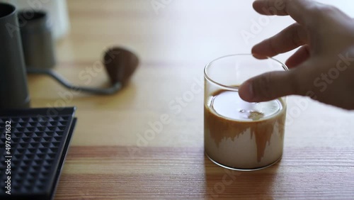 hand of barista grab small cup of chilled latte coffee on wood table