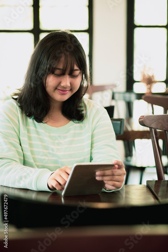 asian younger woman reading message on computer tablet with smiling face