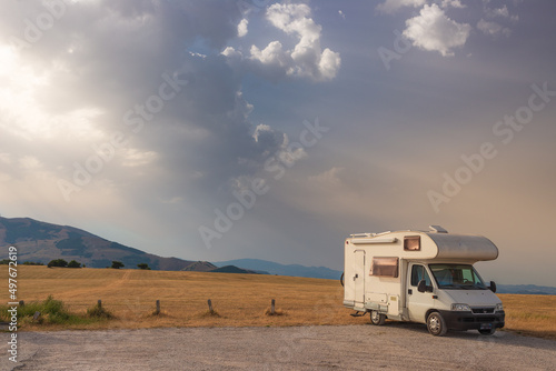 Camper van on road side in beautiful landscape. Dramatic sky at sunset, scenic clouds above unique highlands and hill range in Italy, alternative vanlife vacation concept.