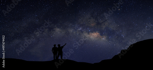 A couple standing on top of a mountain next to the Milky Way galaxy pointing at a bright star. © Jinnawat