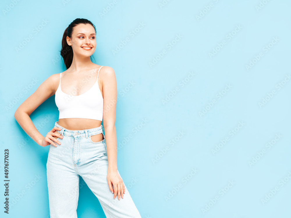 Young beautiful smiling female in trendy summer jeans and top clothes. Sexy carefree woman posing near blue wall in studio. Positive brunette model having fun.Cheerful and happy Young beautiful smiling female in trendy summer jeans and top clothes. Sexy carefree woman posing near blue wall in studio. Positive brunette model having fun.Cheerful and happy