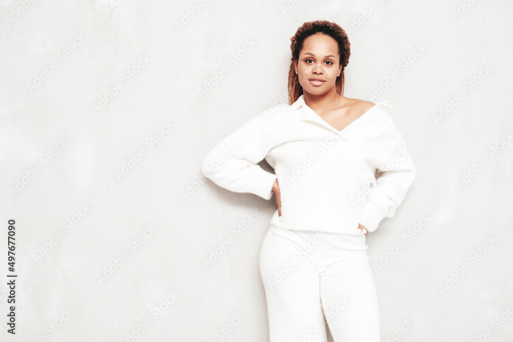 Beautiful black woman with afro curls hairstyle. Smiling model dressed in white summer costume. Sexy carefree female posing near grey wall in studio. Tanned and cheerful. Isolated Beautiful black woman with afro curls hairstyle. Smiling model dressed in white summer costume. Sexy carefree female posing near grey wall in studio. Tanned and cheerful. Isolated