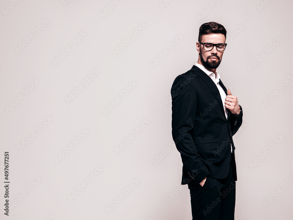 Portrait of handsome confident stylish hipster lambersexual model. Sexy modern man dressed in elegant black suit. Fashion male posing in studio near white wall. Isolated on grey. In spectacles Portrait of handsome confident stylish hipster lambersexual model. Sexy modern man dressed in elegant black suit. Fashion male posing in studio near white wall. Isolated on grey. In spectacles
