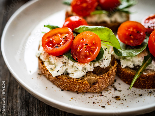 Tasty sandwiches - toasted bread with cream cheese, cherry tomatoes and green leaves on wooden table 