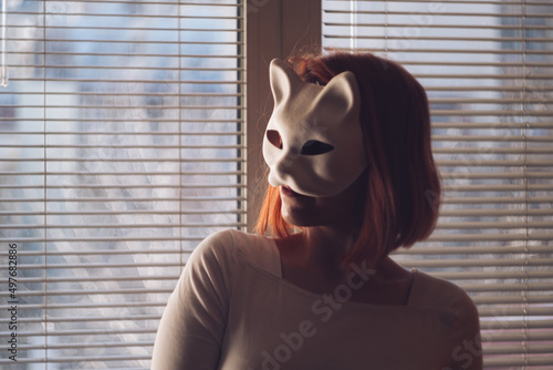 A young and mysterious cat woman with a white face mask portrait by the window blinds