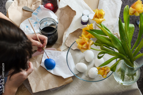 An overhead view of a table where a woman prepares for Easter by dyeing boiled eggs with a dye solution and drying them on a napkin.