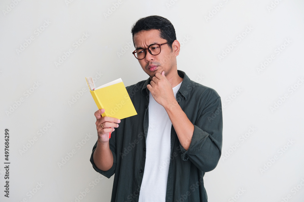 Adult Asian man showing serious face expression while reading a book Adult Asian man showing serious face expression while reading a book