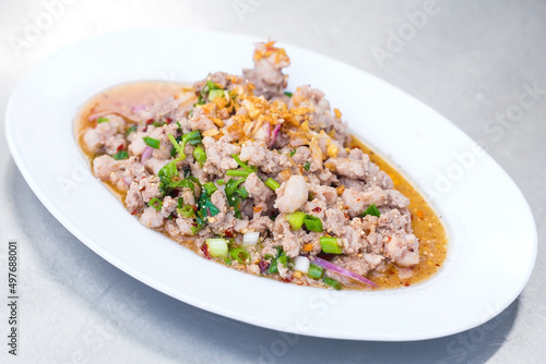 Spicy minced pork salad is traditional food of Northeast of Thailand. It contains minced pork, roasted rice, roasted chili and Thai herbs mixed together. It was put on white plate.
