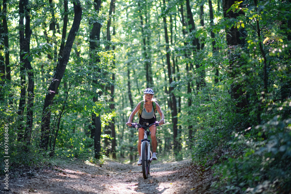 Front view of active senior woman biker cycling outdoors in forest.