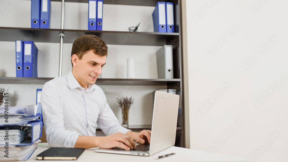 Happy young man office worker auditor accounted in white shirt with rolled up sleeves working on a computer. Happy young man office worker auditor accounted in white shirt with rolled up sleeves working on a computer.