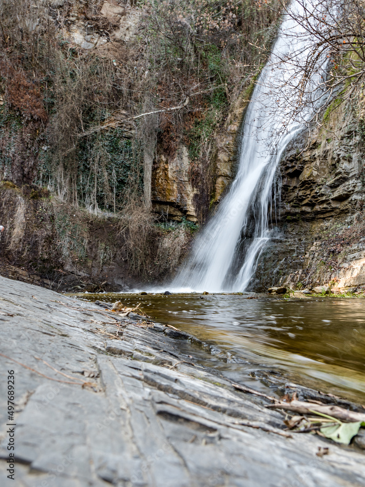 Mountain landscape. The waterfall flows into a mountain river. Around the rock. In the foreground is a huge rock mass. Beautiful waterfall. vertically. Travel. copy space. No people. Mountain landscape. The waterfall flows into a mountain river. Around the rock. In the foreground is a huge rock mass. Beautiful waterfall. vertically. Travel. copy space. No people.