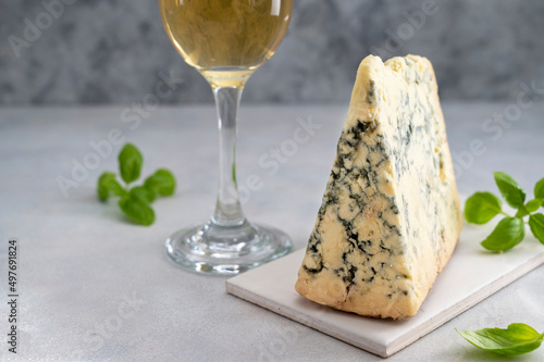Blue cheese piece witha glass of white wine over gray background. One triangle of cheese.