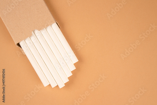 White paper straws in kraft paper box on kight brown background with copy space. Biodegradable drinking straws. Sustainable lifestyle and zero waste concept, mockup image for your design