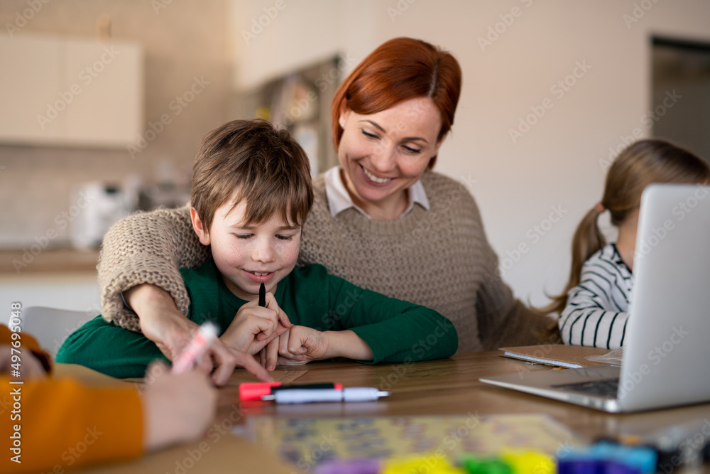 Fototapeta premium Mother of little children working on laptop when distance learning and doing artwork at home.