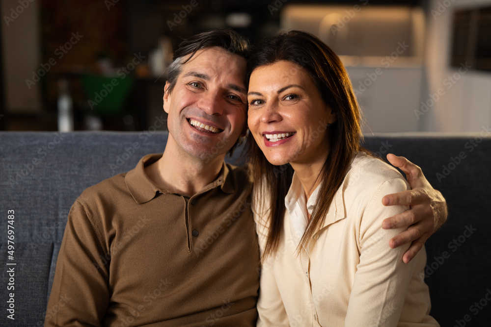 Cinematic shot of young happy married couple is smiling in camera while relaxing and enjoying rest together by leaning on soft comfortable sofa in living room at home. Cinematic shot of young happy married couple is smiling in camera while relaxing and enjoying rest together by leaning on soft comfortable sofa in living room at home.
