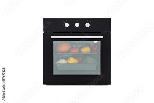 Black oven with closed door and vegetables for roasting, front view, isolated on white