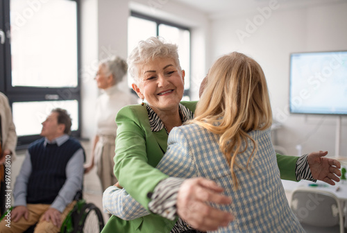 Happy senior women students meeting and hugging in classroom.