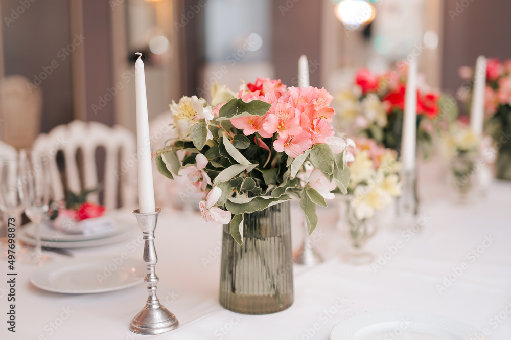 Candles and vase with white roses placed on round table near wineglasses during romantic date in garden Candles and vase with white roses placed on round table near wineglasses during romantic date in garden