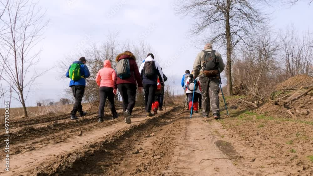 Group of hikers with backpacks walking on rural trail. Active people outdoor. Healthy lifestyle. Cloudy spring day. Back view. Unrecognizable people. Group of hikers with backpacks walking on rural trail. Active people outdoor. Healthy lifestyle. Cloudy spring day. Back view. Unrecognizable people.