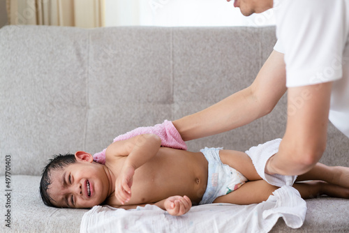 Asian father making tepid sponge for a crying baby boy who get sick and has high fever to reduce body temperature and high fever, concept of parent care to child for sickness at home.