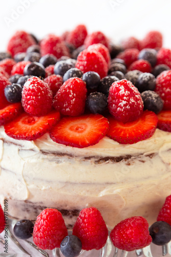 A close up of a chocolate and cream naked cake with strawberries, blueberries and raspberries against a white background.