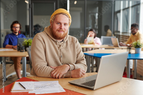 Bild auf Leinwand Portrait of content portly handsome marketing expert in hat sitting at table wit