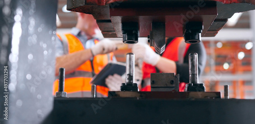 Industrial printing presses with metal factory engineers are inspect the finished metal forming at the back.