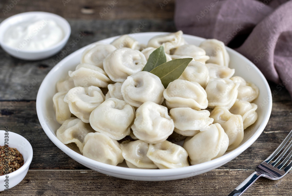Russian dumplings, pelmeni with meat, sour cream, black pepper,bay leaf on wooden background, side view. Selective focus Russian dumplings, pelmeni with meat, sour cream, black pepper,bay leaf on wooden background, side view. Selective focus