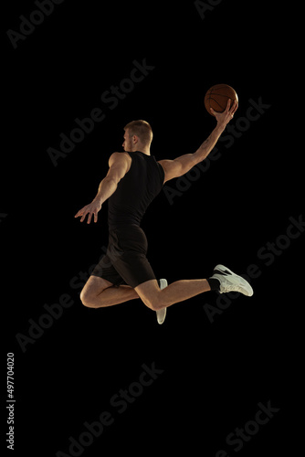 Dynamic portrait of young man, basketball player in black uniform training isolated on dark background. Achievements, sport career, motion concepts.