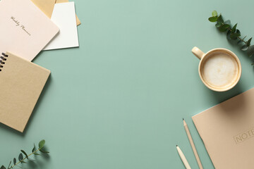 Aesthetics minimal workspace with paper notebooks, coffee cup, eucalyptus leaves on green table. Flat lay, top view
