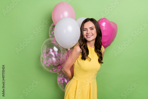 Portrait of attractive cheerful wavy-haired girl hiding air balls occasion isolated over bright green color background
