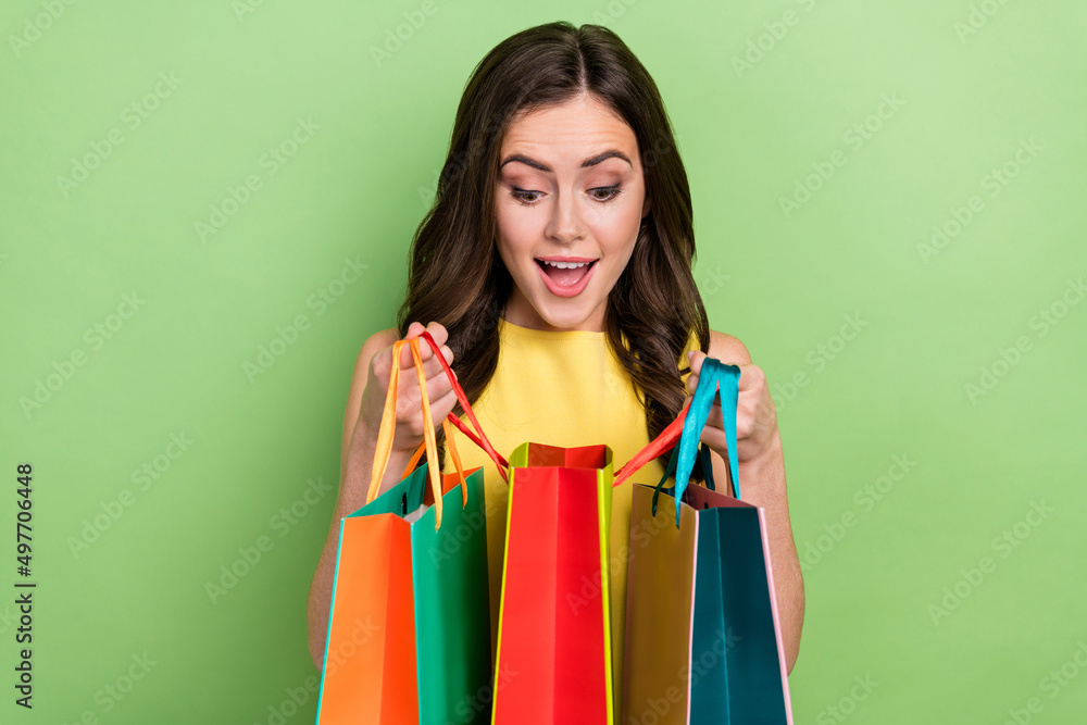 Portrait of attractive girly cheerful wavy-haired girl looking inside bags new things isolated over bright green color background