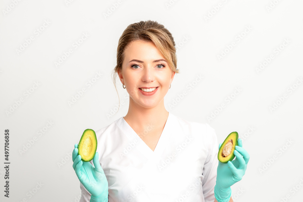 Portrait of smiling young female nutritionist doctor with organic avocado fruits posing at camera on white background, copy space. Benefits of proper nutrition Portrait of smiling young female nutritionist doctor with organic avocado fruits posing at camera on white background, copy space. Benefits of proper nutrition