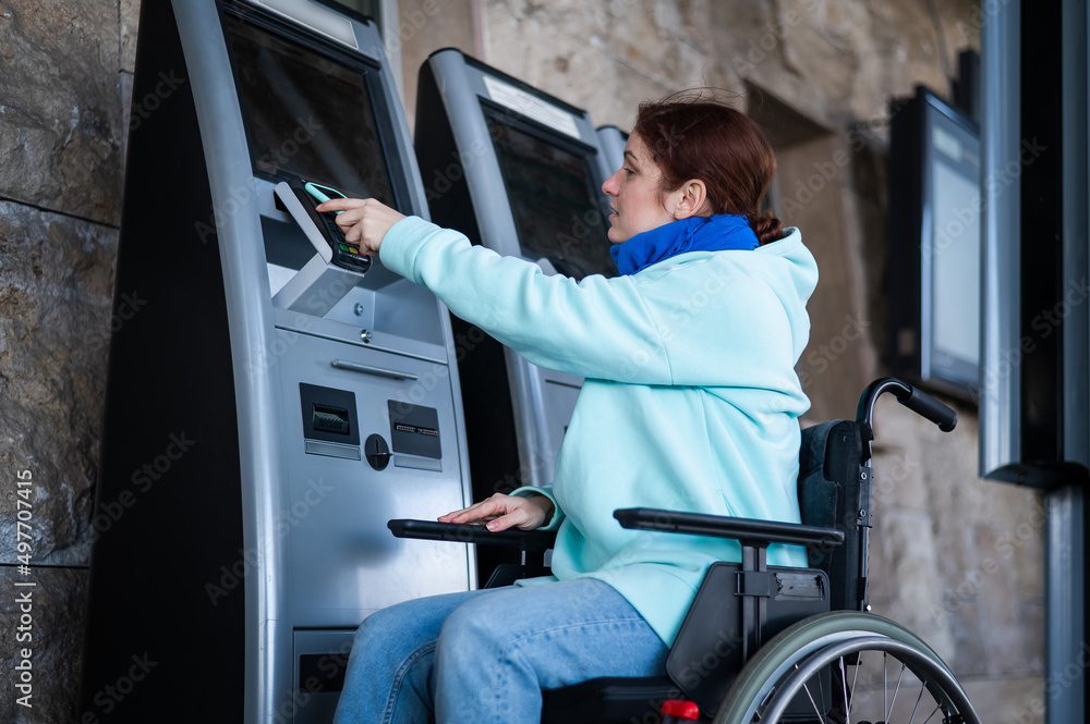 Caucasian woman in a wheelchair buys a train ticket using a mobile phone at a self-service checkout. Caucasian woman in a wheelchair buys a train ticket using a mobile phone at a self-service checkout.