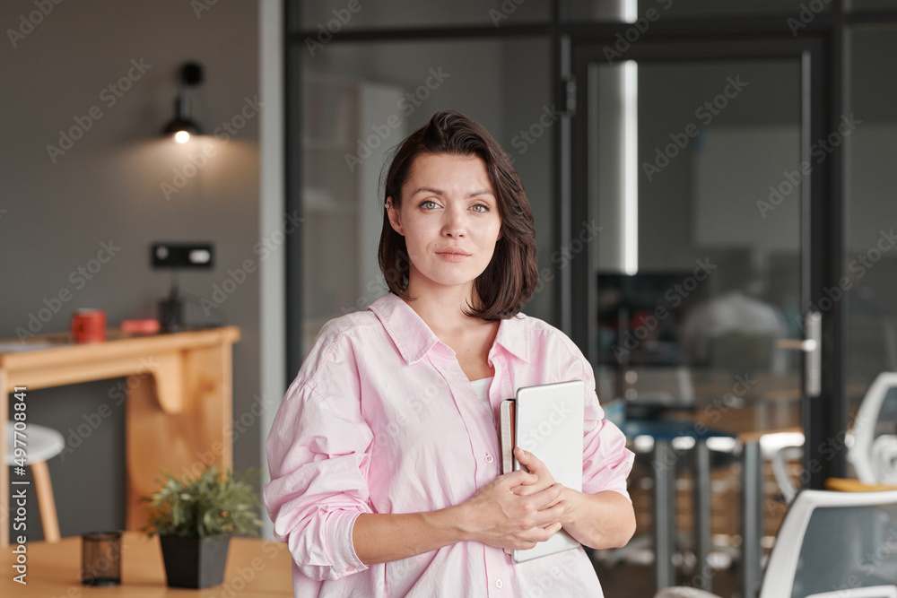 Portrait of content beautiful young Caucasian office woman in pink shirt holding tablet and planner in modern office Portrait of content beautiful young Caucasian office woman in pink shirt holding tablet and planner in modern office