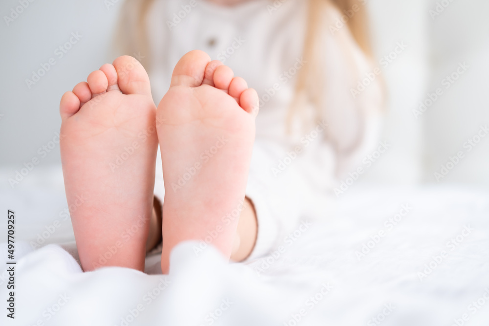 Close up kid child barefooted legs feet lying on white bed linen. Neutral pastel light color tones Close up kid child barefooted legs feet lying on white bed linen. Neutral pastel light color tones