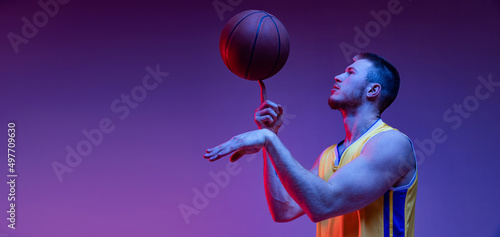 Spin. Studio shot of muscled man, basketball player training with ball isolated on purple background in neon light. Goals, sport, motion, activity concepts.