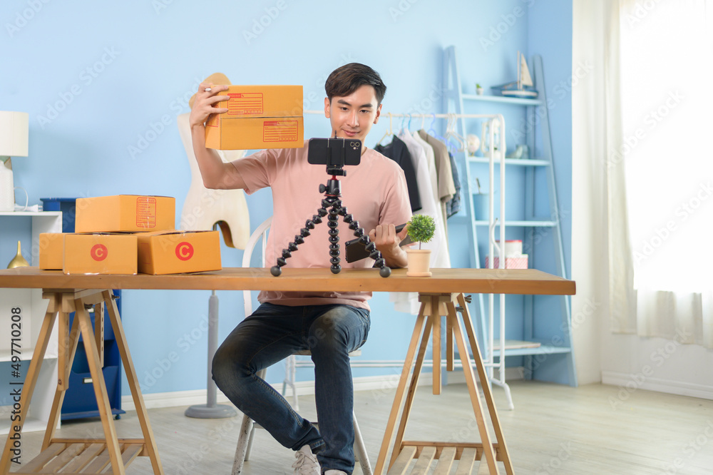 An Asian man is showing clothes in front of smartphone  live streaming at his shop. Technology online business concept.