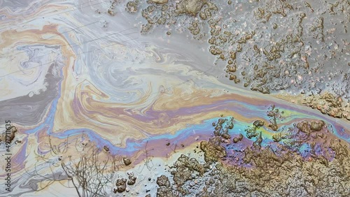 A multicolored spot from oil or gasoline spreads over a puddle on the asphalt. The problem of ecology and water pollution in the metropolis. photo