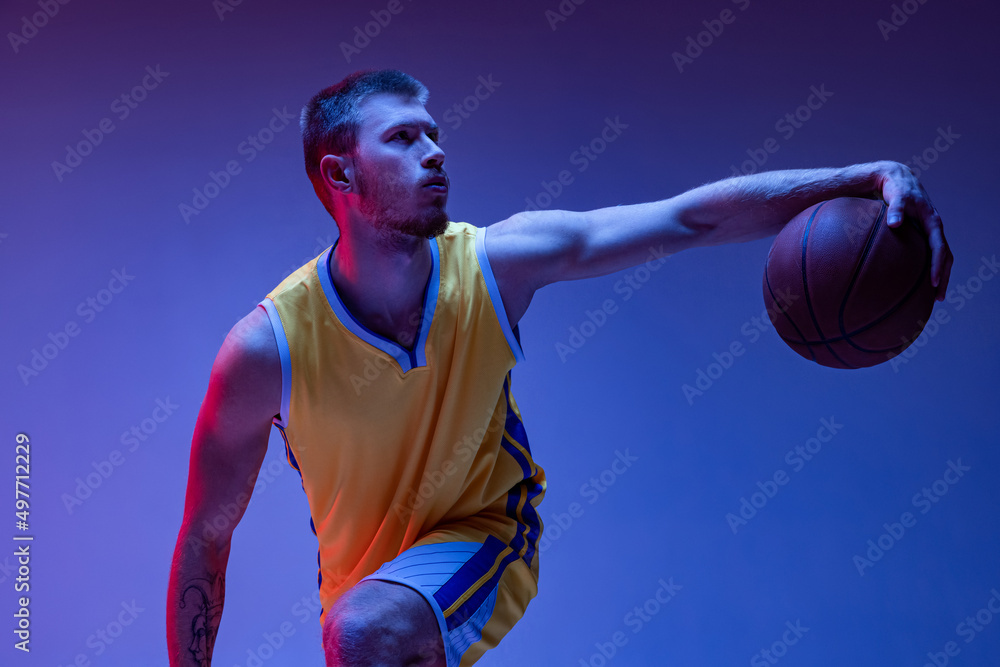 Young man, professional basketball player training with ball isolated on purple background in neon light. Goals, sport, motion, activity concepts. Young man, professional basketball player training with ball isolated on purple background in neon light. Goals, sport, motion, activity concepts.