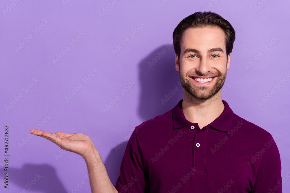 Photo of nice young brunet guy hold empty space wear violet t-shirt isolated on purple color background Photo of nice young brunet guy hold empty space wear violet t-shirt isolated on purple color background