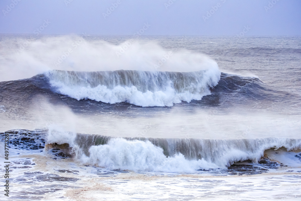 Big waves crashing on the sea with greenish blue color during a cloudy day