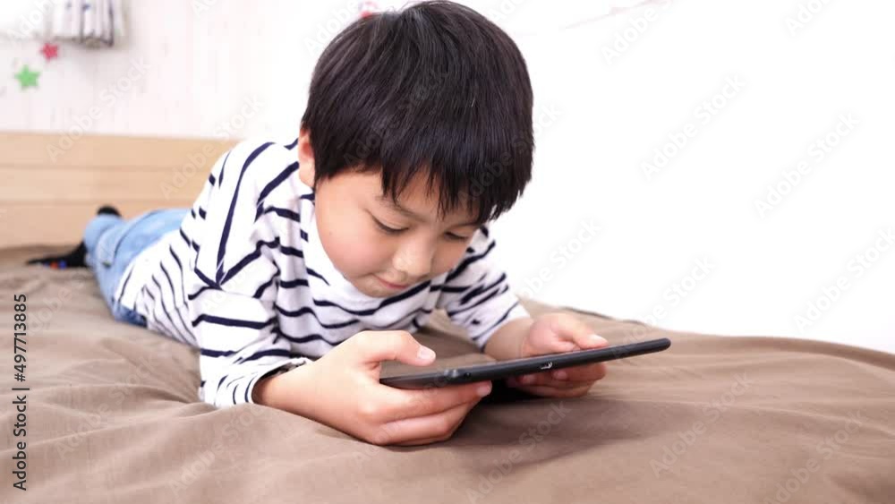 ベッドでタブレット端末を見ているアジア人の男の子 ベッドでタブレット端末を見ているアジア人の男の子