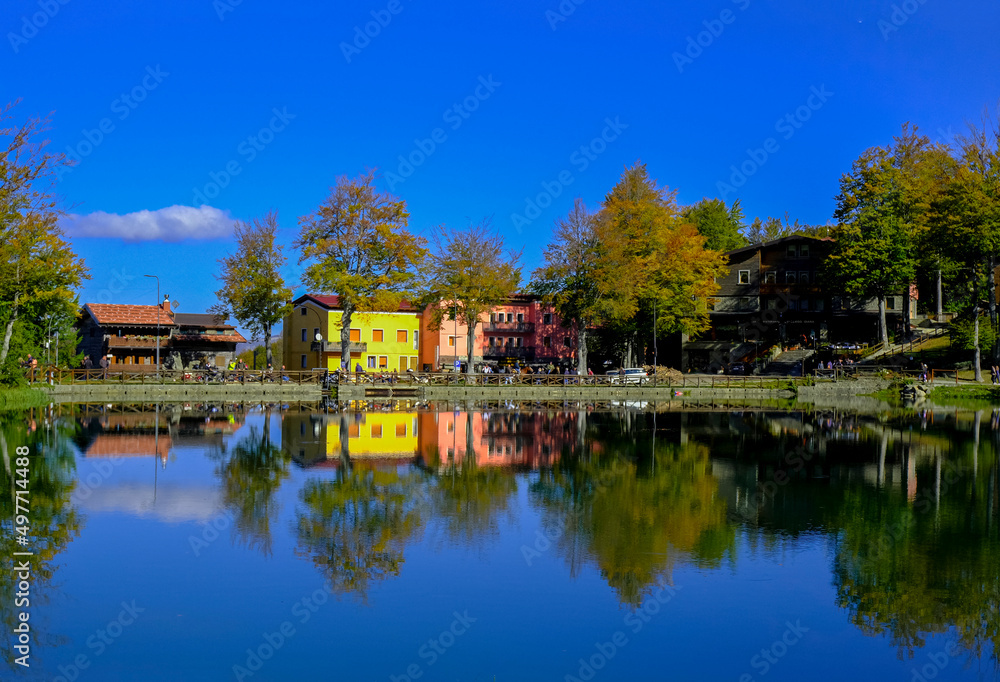 Colorful houses on the lake on a sunny bright day. Water reflections. Landscape background. Cerreto Laghi, Reggio Emilia, Italy. Travel 