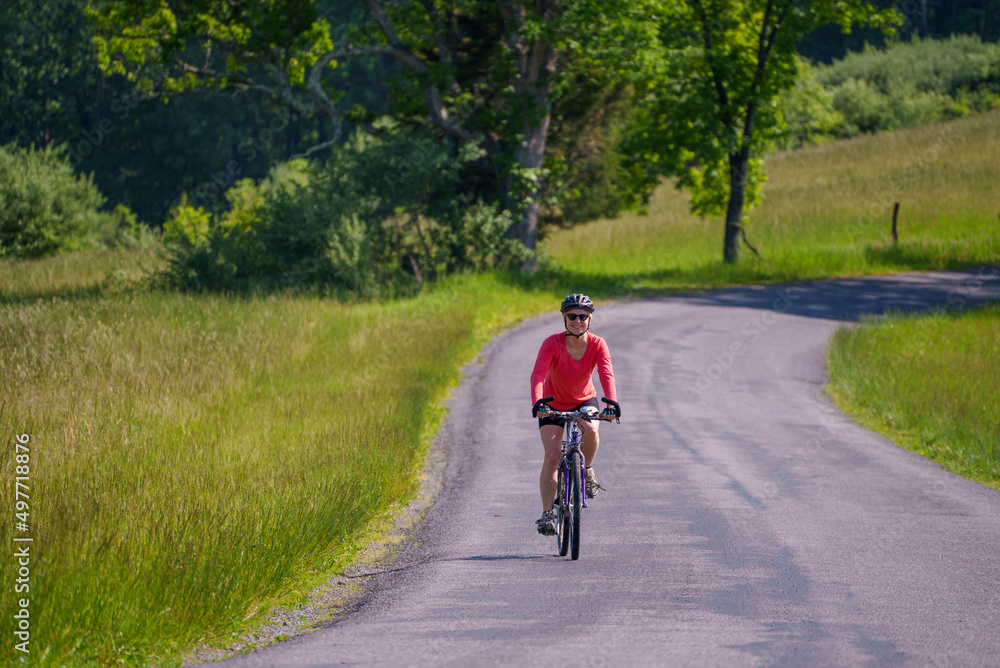 Smiling, active, mature woman wearing bike helmet biking on a country road on a spring summer day.