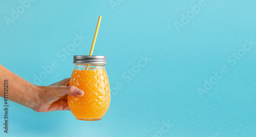 Female hand holding fresh smoothie jar on blue background. Healthy eating, copy space.