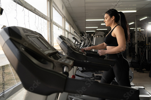 Side view of caucasian woman in sportswear adjusting speed on treadmill while exercising at gym or sport club © mtrlin