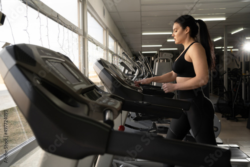 Side view of caucasian woman in sportswear adjusting speed on treadmill while exercising at gym or sport club