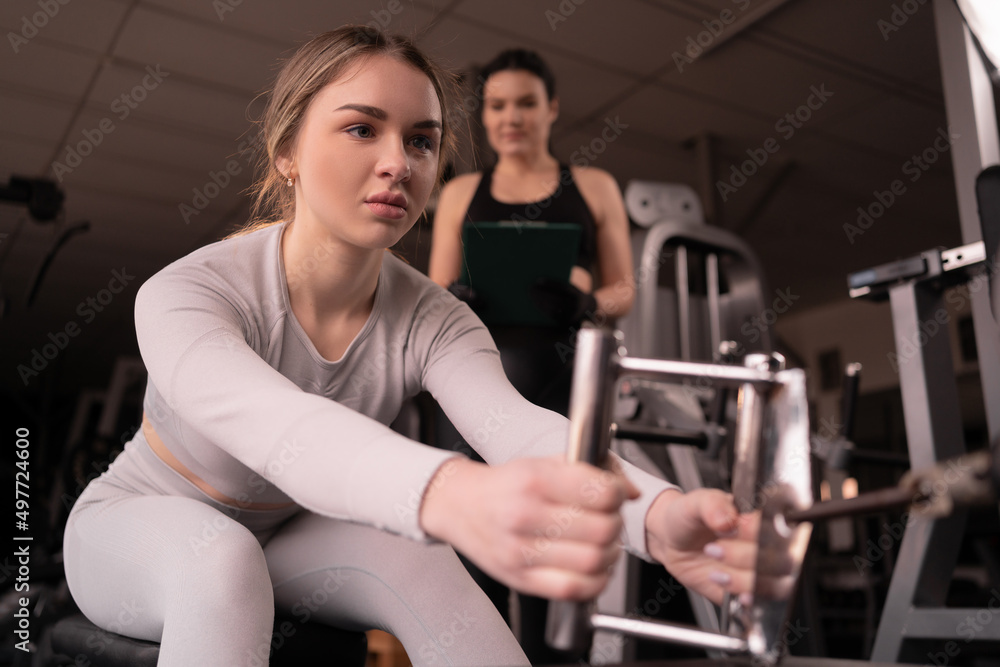 portrait of a woman in a health club with her personal trainer learning proper technique on a weight lifting machine pulling machine in a fitness club. portrait of a woman in a health club with her personal trainer learning proper technique on a weight lifting machine pulling machine in a fitness club.